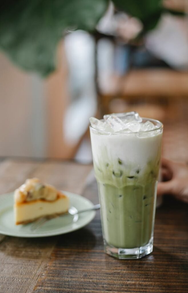 Glass of tasty refreshing matcha latte served on table with yummy pie slice in cafe